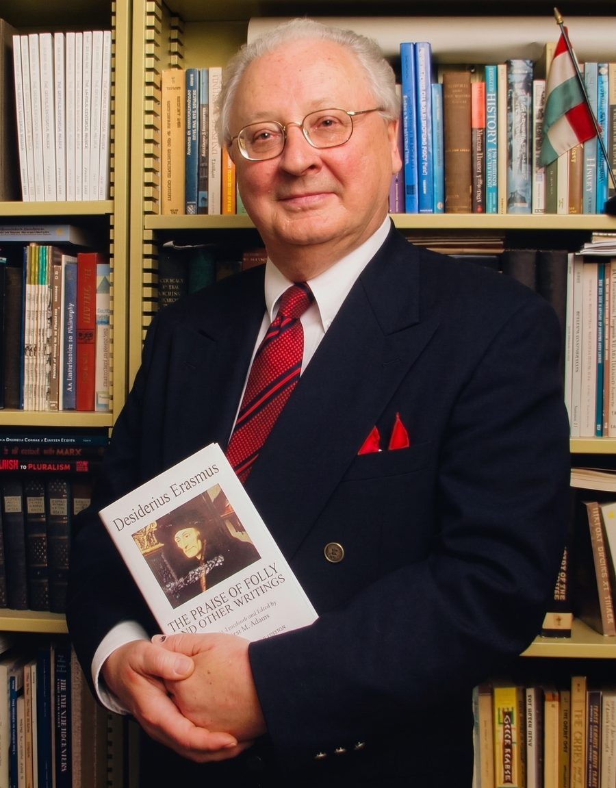 Dr. Leslie S. Domonkos in his study, holding a volume of Erasmus, with a Hungarian flag on the shelf behind him.