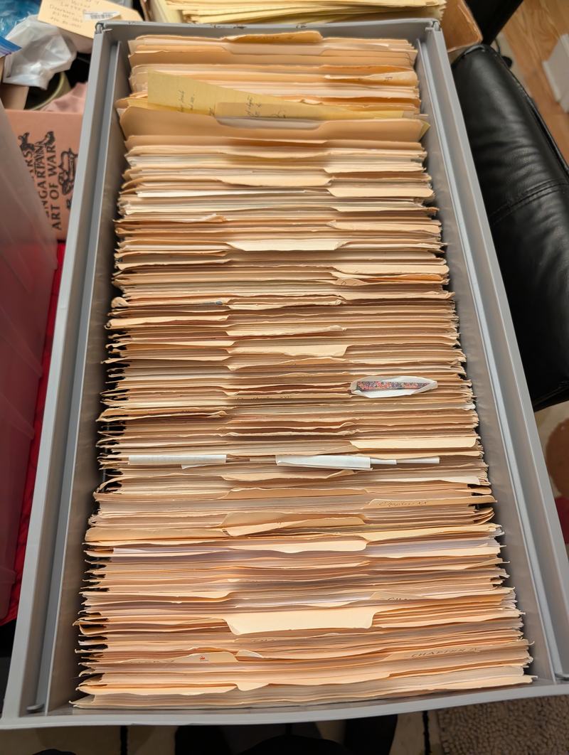 A filing cabinet drawer packed with manila folders, several labelled by chapter in roman numerals.