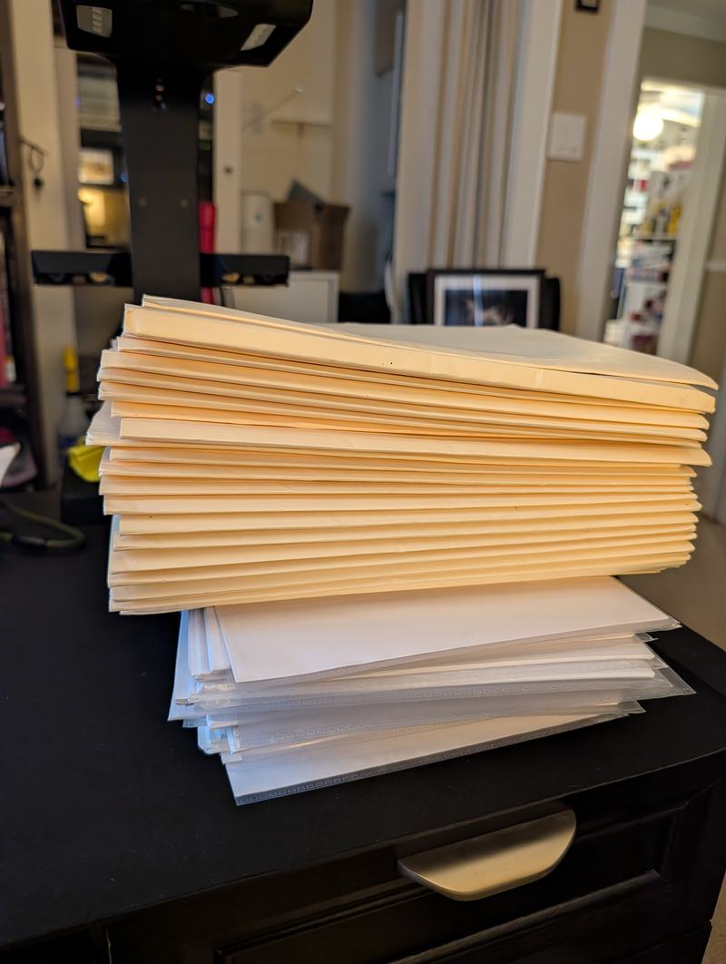 A tall stack of manila envelopes and sleeves standing beside a document scanner.