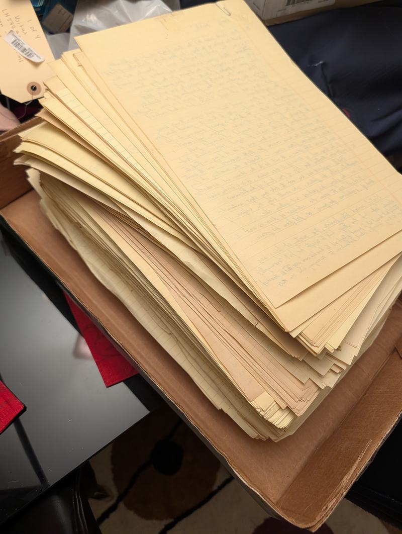 A stack of handwritten yellow manuscript pages on a box bearing a luggage tag.