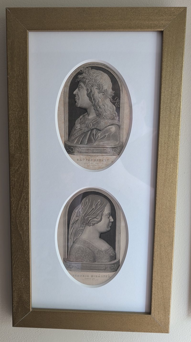 Two oval steel engravings framed one above the other behind a single white mat: above, the profile of a long-haired man in a laurel wreath and jewelled collar; below, the profile of a veiled woman in an embroidered gown. Both are engraved to look like marble reliefs set in arched niches.